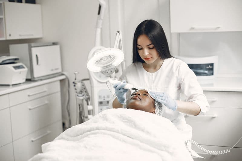 Aesthetician providing professional facial treatment to client in modern spa clinic — microneedling vs PRP comparison