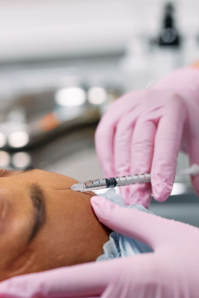 Aesthetic nurse administering Botox injection to patient forehead in clinical setting