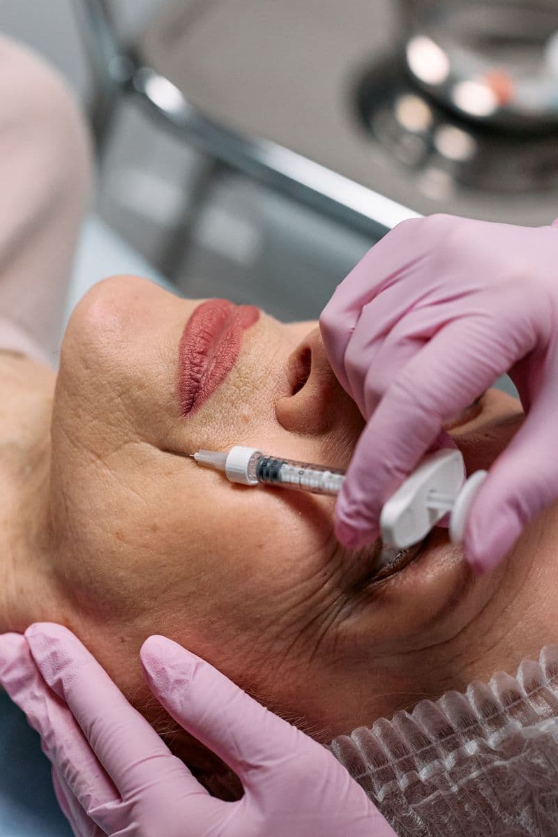 Beautician administering dermal filler injection to woman's face in aesthetic clinic