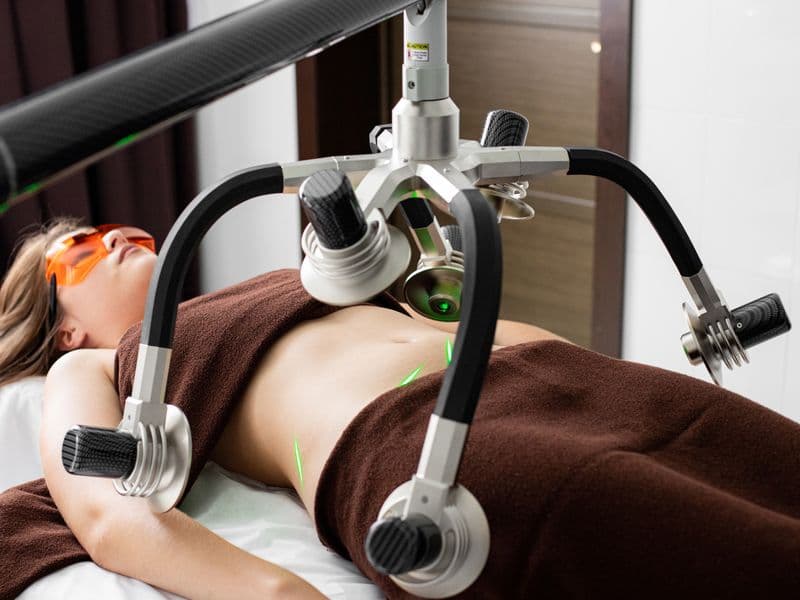 Female patient lying under laser body contouring machine at medical clinic — CoolSculpting aftercare guide